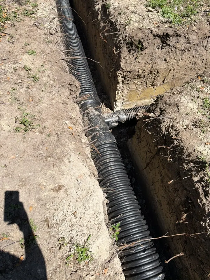 A black corrugated drainage pipe junction in an open trench