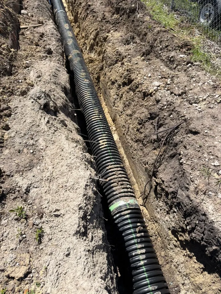 Black drainage pipe extending along an open outdoor trench